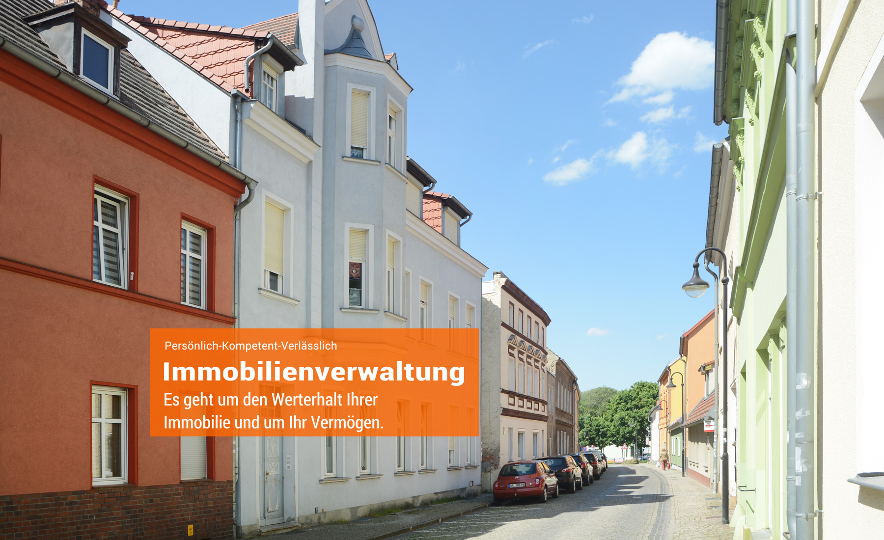 Straße einer Kleinstadt mit hellen Häusern und parkenden Autos