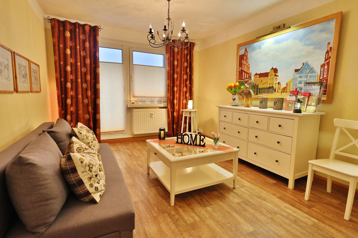 Gästewohnung Goldborn, helles Wohnzimmer mit Ecksofa, Tisch, Sideboard und Bildern an den Wänden, Blick zum Balkon